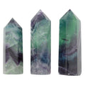Three faceted crystal point towers in natural fluorite, featuring marbled patterns of green, purple, and gray, displayed against a solid white background.