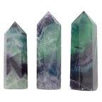 Three faceted crystal point towers in natural fluorite, featuring marbled patterns of green, purple, and gray, displayed against a solid white background.