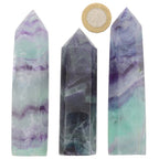 Three pointed fluorite crystal towers of varying colors and patterns, with a British coin placed above the center tower for scale, on a plain white background.