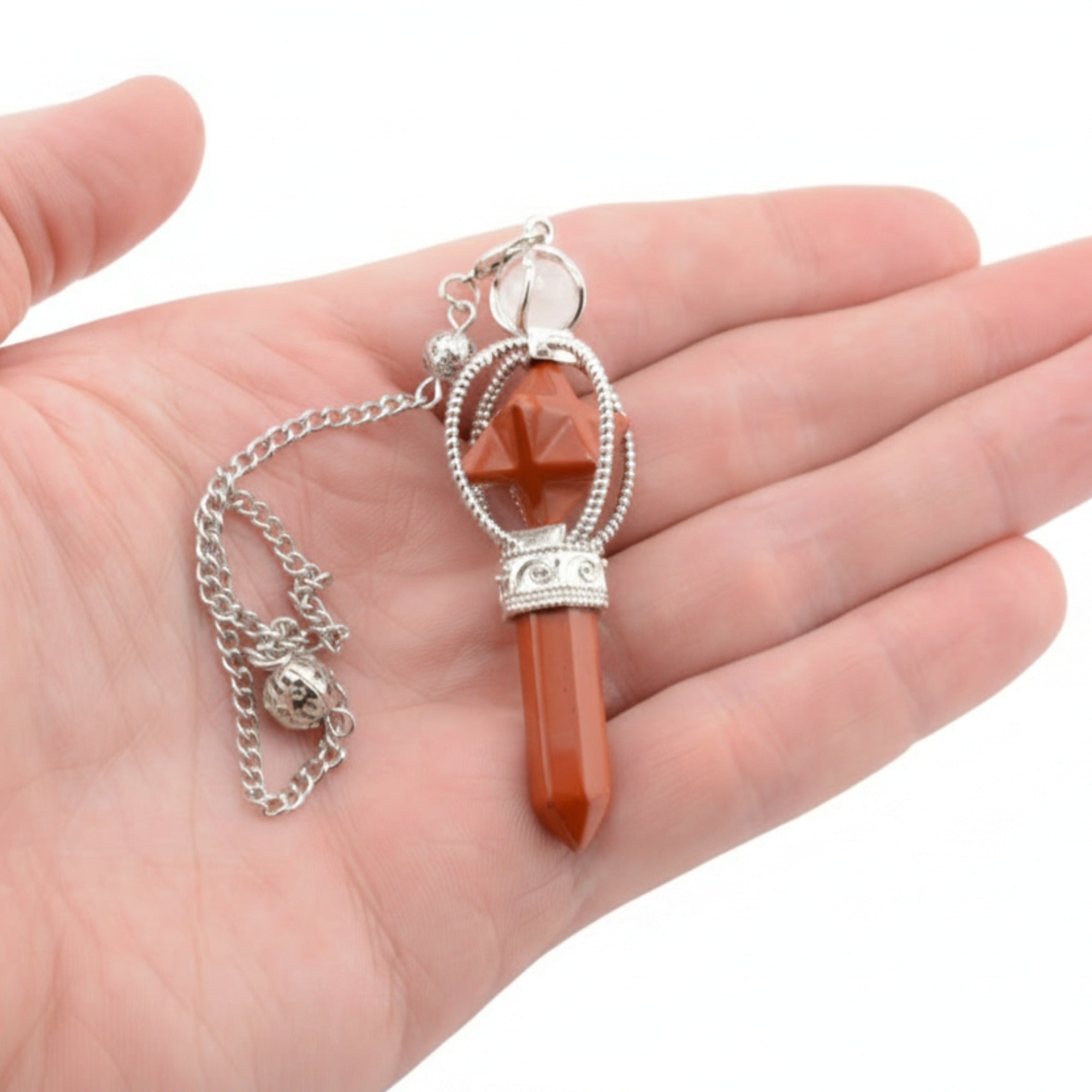 A Red Jasper Pendulum with a point and merkaba. Includes a silver coloured chain and ball. A hand is holding it on a white background