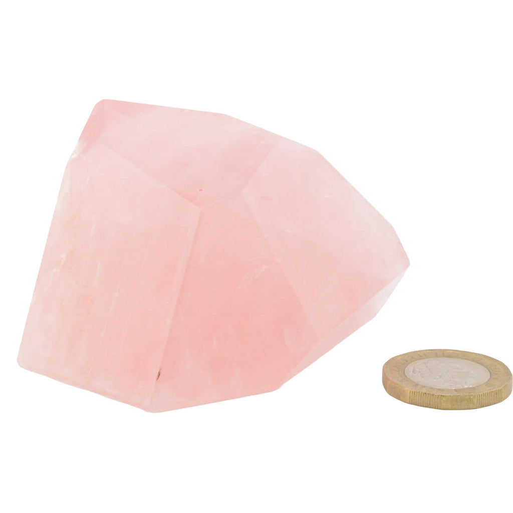A rose quartz crystal polished freeform, shown on a plain white background next to a small gold coin for scale.