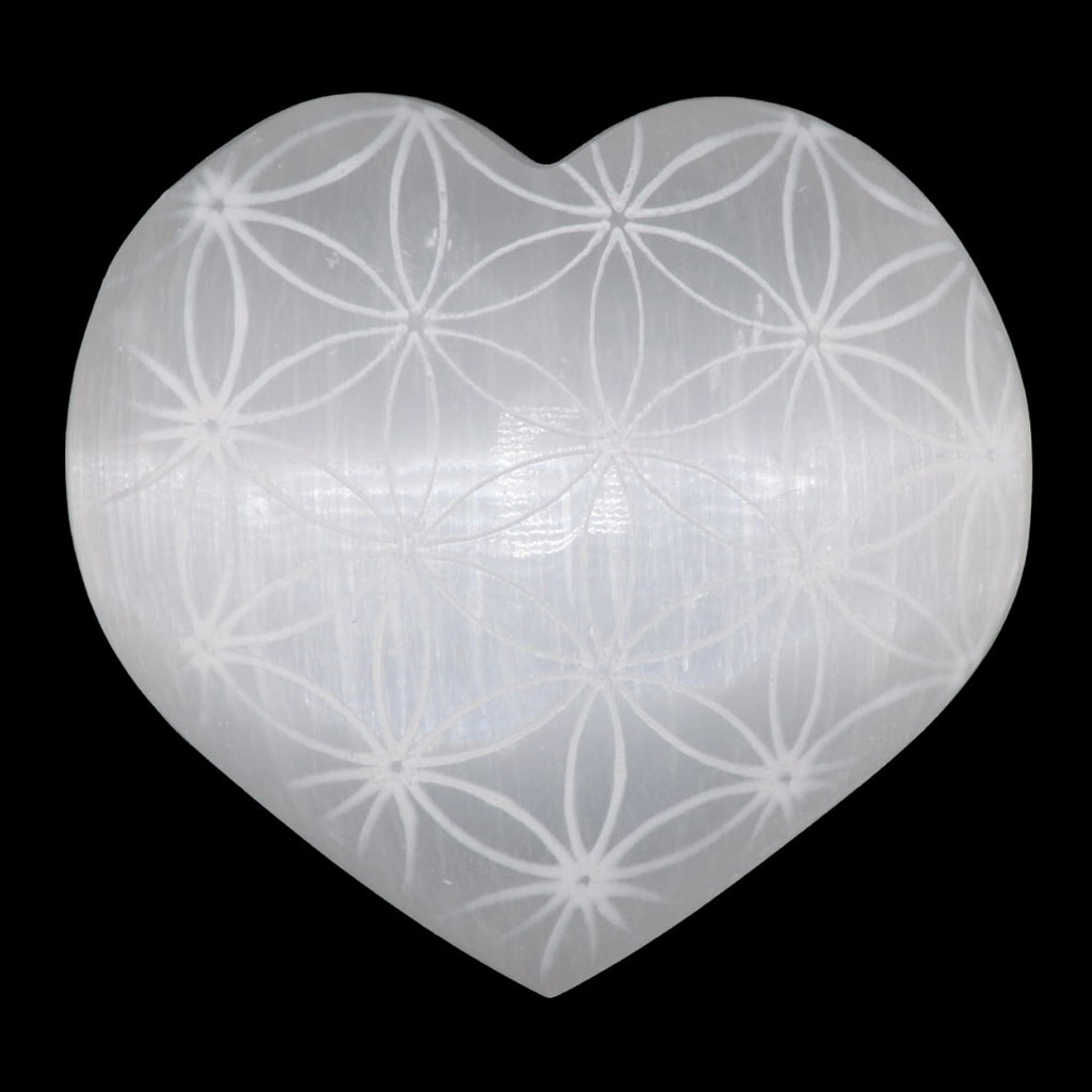 A heart-shaped translucent selenite carving with a white engraving of the flower of life, shown against a solid black background.