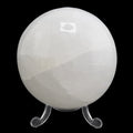 A polished white selenite sphere on a clear acrylic stand, photographed against a solid black background.