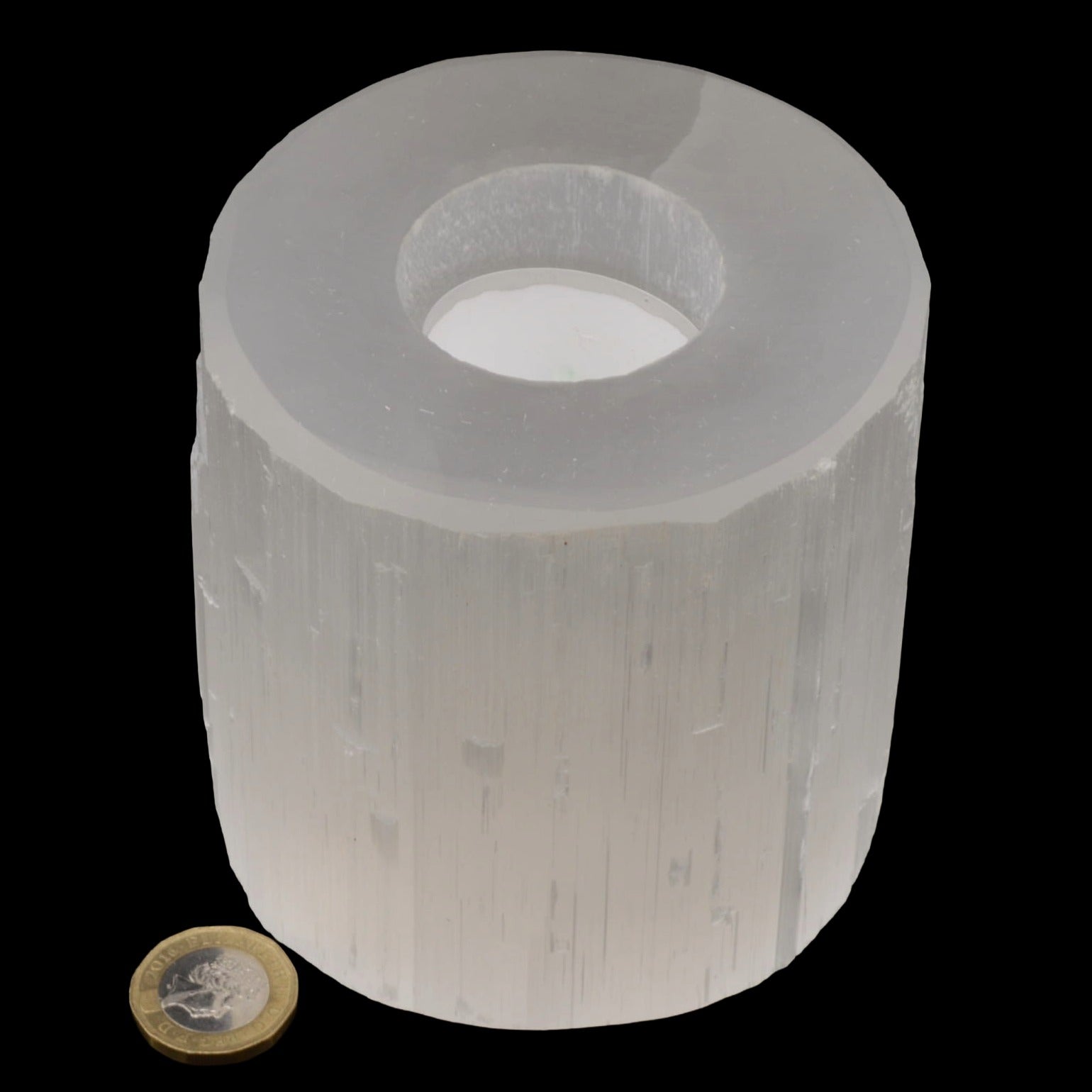 Natural selenite tea light holder with a coin for scale. Shown on a pure black background