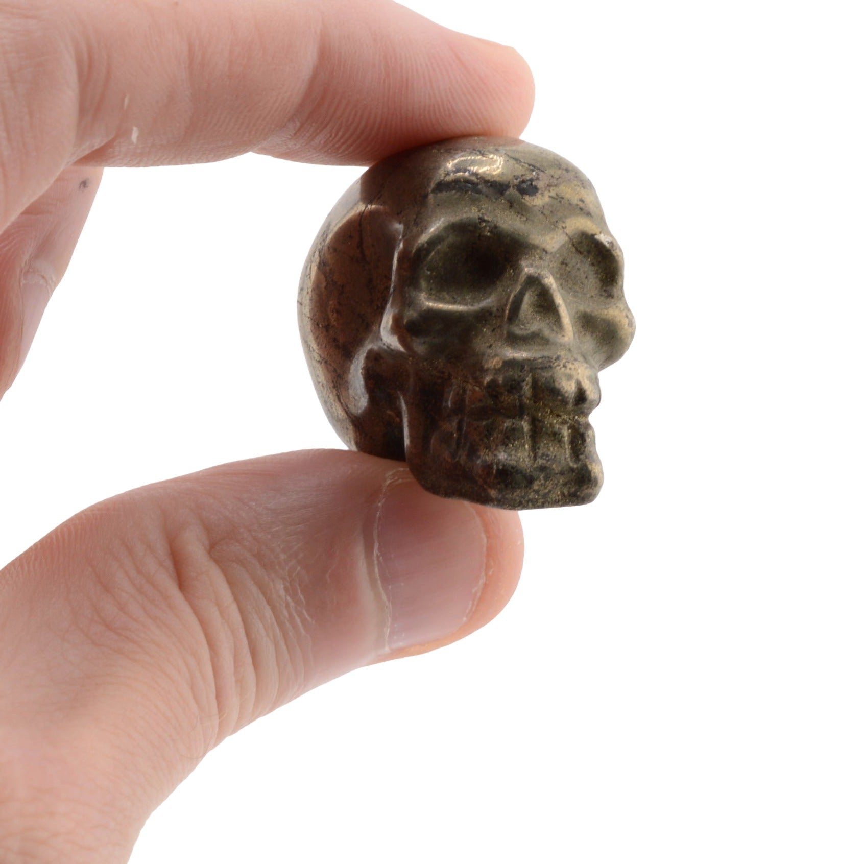 A small carved pyrite skull-shaped object held between a person's fingers against a plain white background.