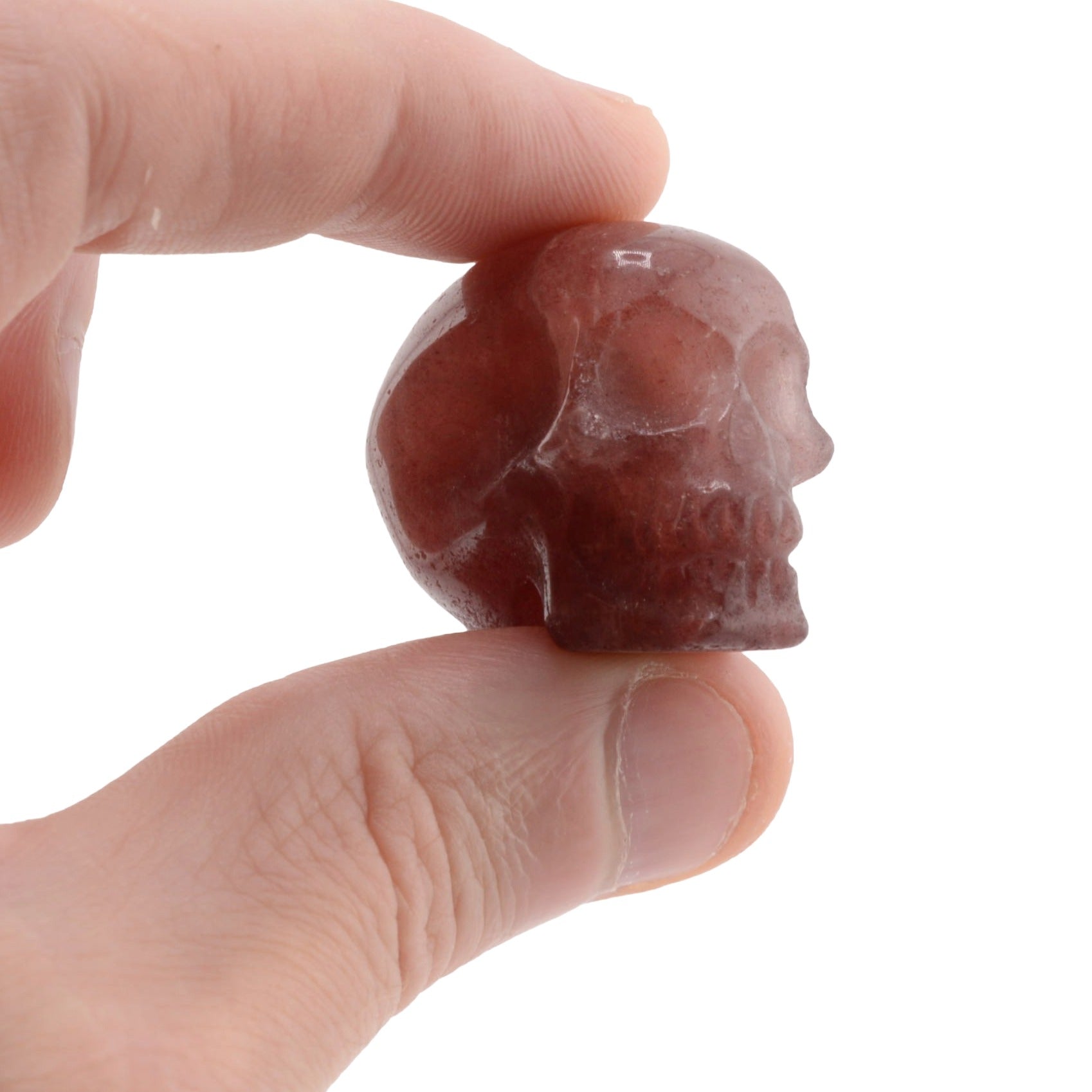 A small carved skull raspberry adventurine gemstone held between two fingers against a plain white background.