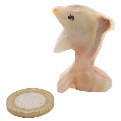 A small carved figurine of a jumping dolphin made from banded calcite, shown next to a UK pound coin for scale on a white background.