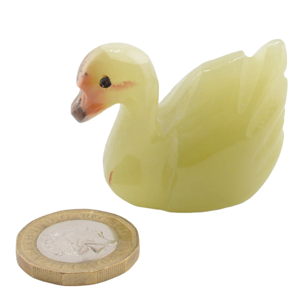 A small swan figurine, made from banded calcite shown next to a UK pound coin for scale, on a plain white background.
