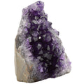 A natural amethyst crystal geode specimen with a cluster of purple and lavender crystalline points rising from a rough, earthy gray-brown matrix, shown on a plain white background.