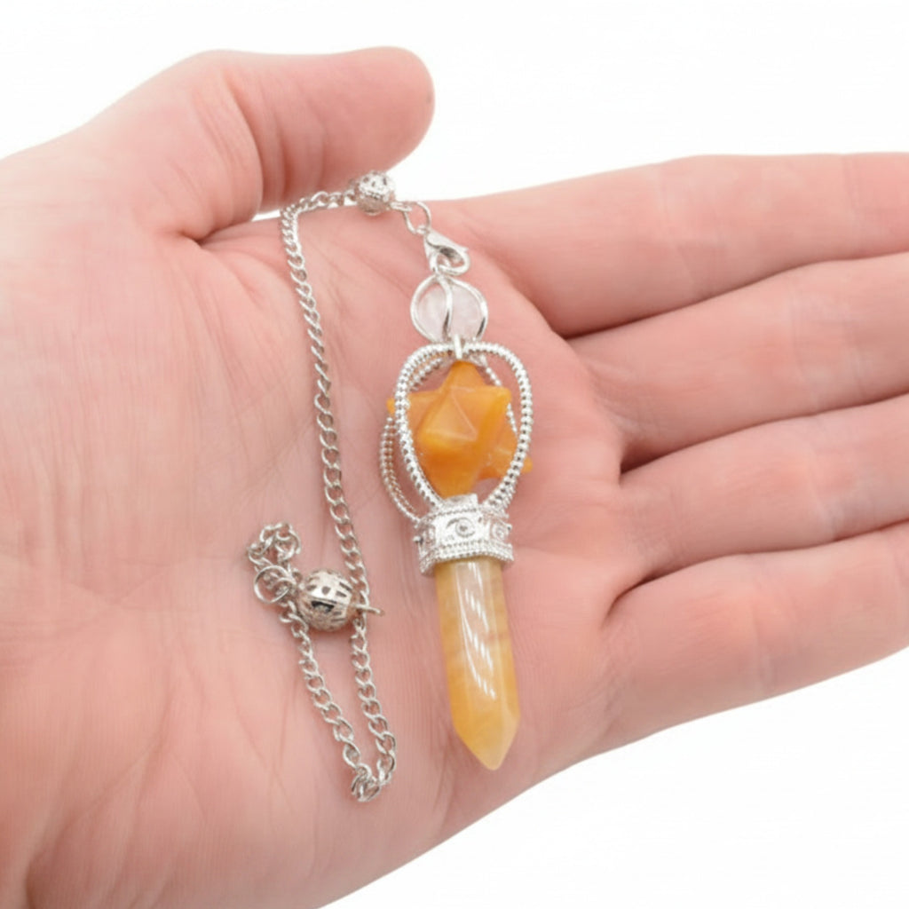 A silver-toned pendulum necklace with a carved yellow-orange crystal point and a faceted orange gemstone, displayed on a person's open hand against a white background.